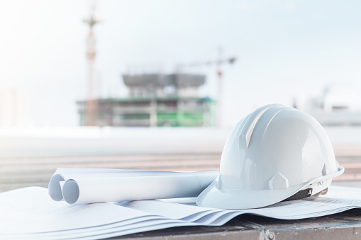 The white safety helmet and the blueprint at construction site with crane background