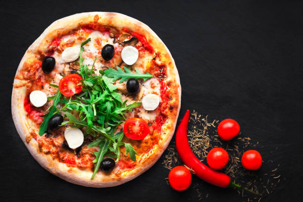 istock Rustic pizza with mozzarella, four cheese, olives and arugula  top view with copy space for restaurant menu on black background. 695743966