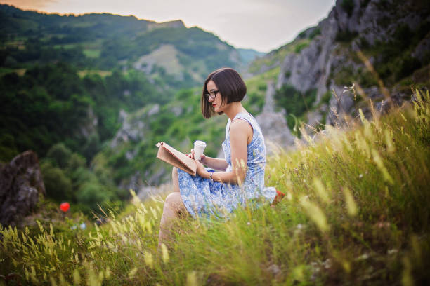 istock Relaxed, young woman reading book on green grass 695744004
