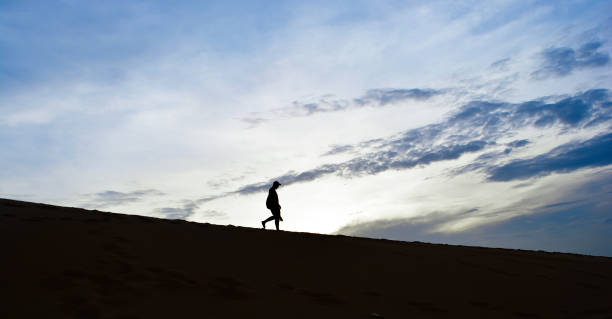 istock Silhouette man walking down desert  with clouds blue sky background in the morning 695745260