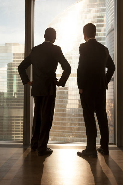 istock Two diverse multi-ethnic partners standing near window, vertical rear view 695760070