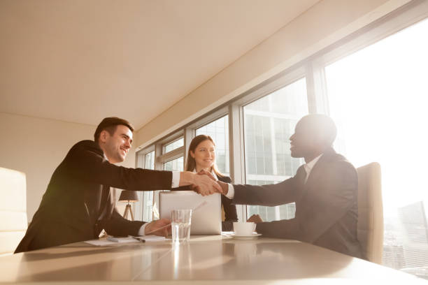 istock Cheerful black and white businessmen shaking hands at multi-ethnic meeting 695760194