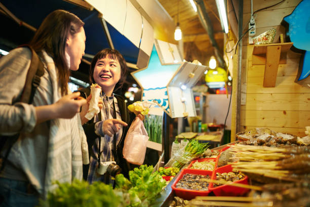 Let's eat Shot of two young women eating food at a Taiwanese night market taiwan people stock pictures, royalty-free photos & images