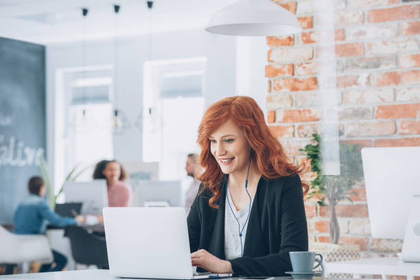Businesswoman smiling working on laptop Beautiful businesswoman with headphones smiling working on laptop in coworking studio box office photos stock pictures, royalty-free photos & images