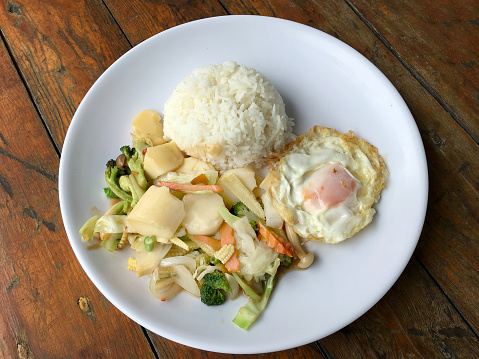 Sauteed mixed vegetables n oyster sauce with rice and fried egg on white plate. Thai food.