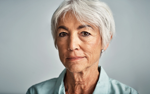 Closeup portrait smiling confident senior woman sitting on comfortable sofa at home. Happy retired female with stylish gray hair, white teeth looking away. Natural beauty, healthy lifestyle concept