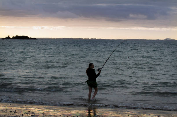 Young woman fishing at the beach during sunset.