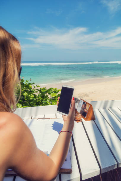 istock Girl using cellphone in the coffee shop on a tropical exotic beach. 695786018