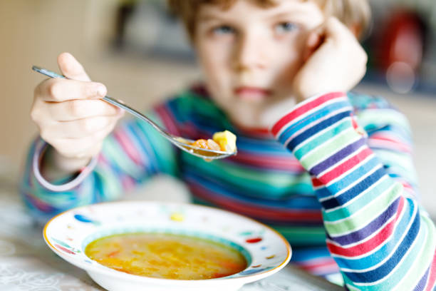 istock Adorable little school boy eating vegetable soup indoor. 695792670