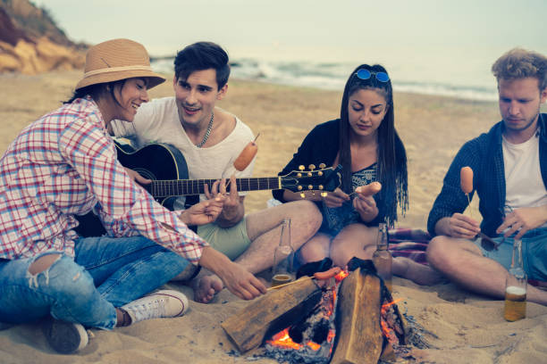 istock friends sitting on stones on beach. man is playing guitar. 695806282