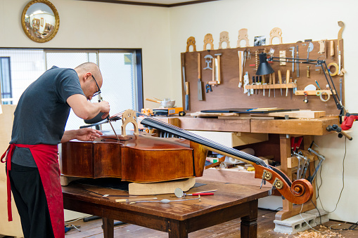 Repairman inspecting vintage double bass in his workshop. Tokyo, Japan. May 2017