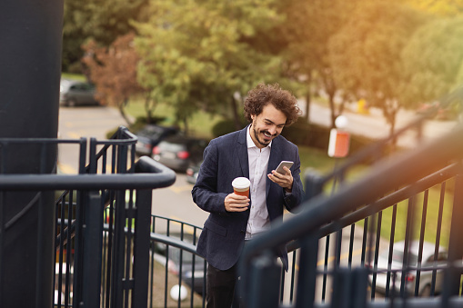 Smiling businessman with smart phone and coffee cup walking outdoors