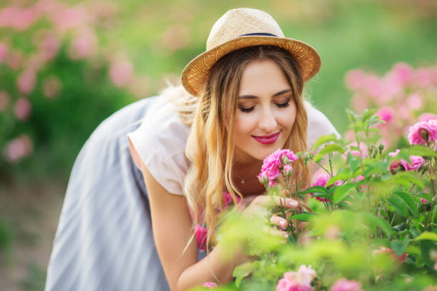 Beautiful young woman with hat is smelling roses in a garden stock photo