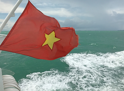 The flag of Vietnam (red flag with a gold star) fluttering on the ship's end in the sea, Vietnam.
