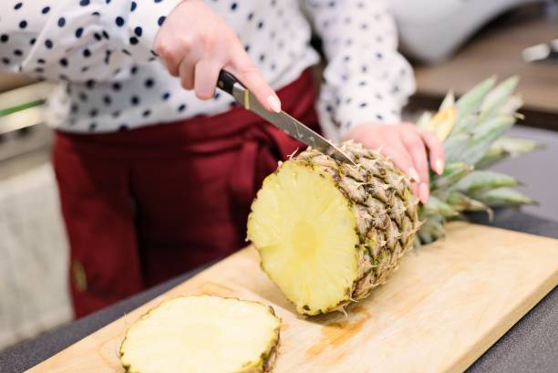 istock Woman, cafe worker slicing pineapple at the cutting board 695854042