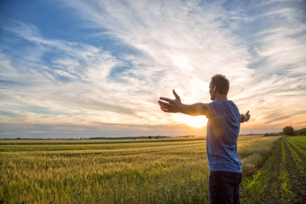 istock Man standing in an open field at sunset with open arms - embracing nature 695854668