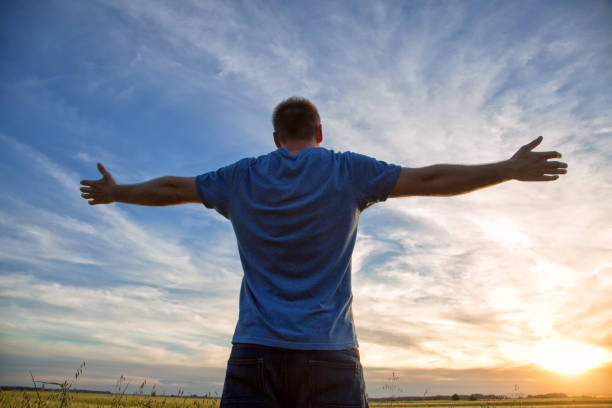 istock Man standing in an open field at sunset with open arms - embracing nature 695854888