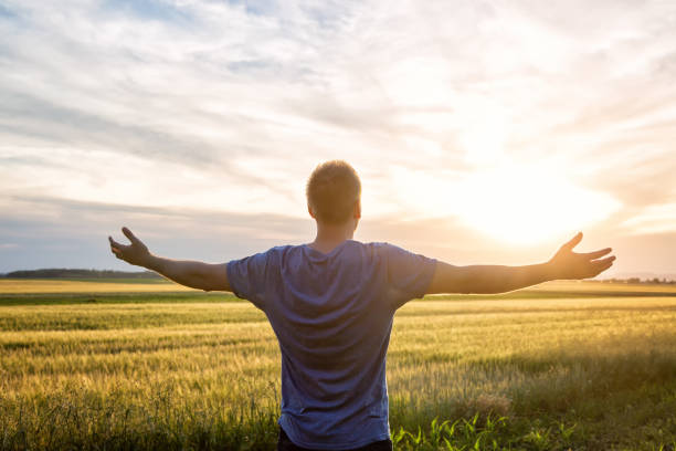 istock Man standing in an open field at sunset with open arms - embracing nature 695855262