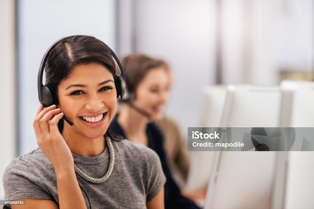 Is there anything else I can help with? Portrait of a call centre agent working in an office with her colleagues in the background Contact Us Stock Photo