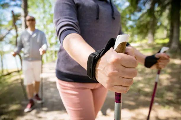 Nordic walking, hand close-up. Man and mature woman hiking in green sunny forest. Active people outdoors. Scenic peaceful Finnish summer landscape.