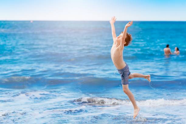 istock Happy child jumping and playing on the beach 695901332