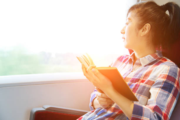 istock Young woman reading book on a train 695904528