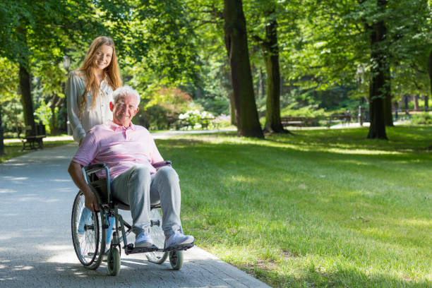 Woman with grandfather on a wheelchair in the park Smiling woman with grandfather on a wheelchair during walk in the park united states senate committee on health education labor and pensions stock pictures, royalty-free photos & images