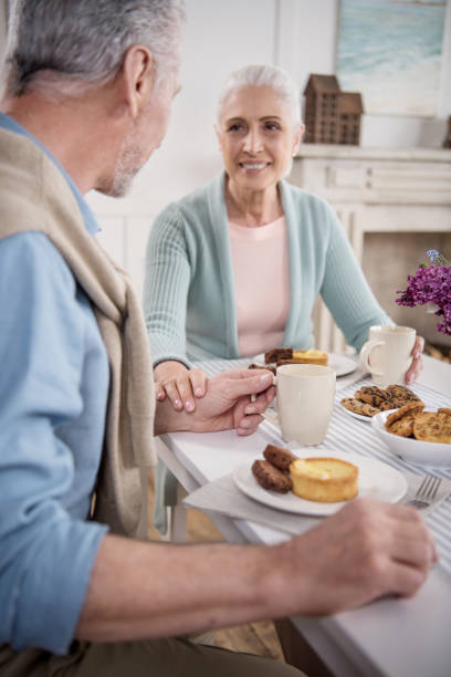 istock elderly couple holding hands while having breakfast at home 695915266