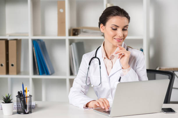 istock pensive young caucasian doctor looking at laptop screen while sitting at table in professional clinic 695916780