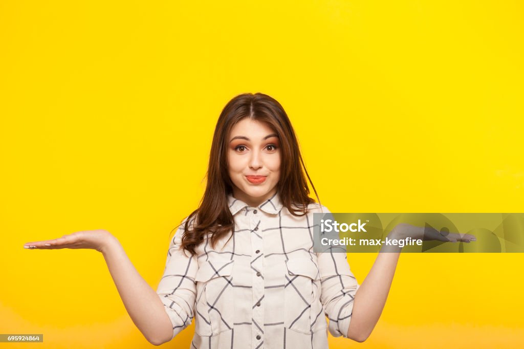 Woman gesturing in embarrassment Young girl in shirt holding hands apart in gesture of confusion and smiling at camera on yellow. Women Stock Photo