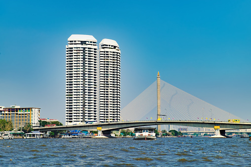 Bangkok, Thailand - December 22, 2015: People travelling by boat in Chao Phraya river, overlooking the modern Bangkok with skyscrapers and The Rama VIII bridge, Thailand