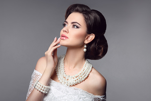 Beauty bride makeup. Elegant fashionable woman portrait. Retro hair style. Brunette model with pearls jewelry women set present isolated on grey studio background.