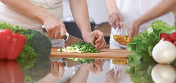 istock Close-up of four human hands are cooking in a kitchen. Friends having fun while preparing fresh salad. Vegetarian, healthy meal and friendship concept 695940046