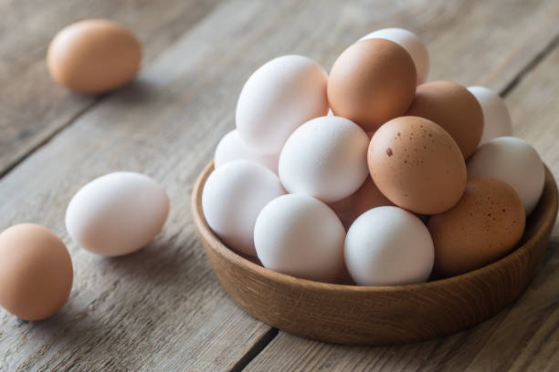 Wooden bowl of raw chicken eggs stock photo