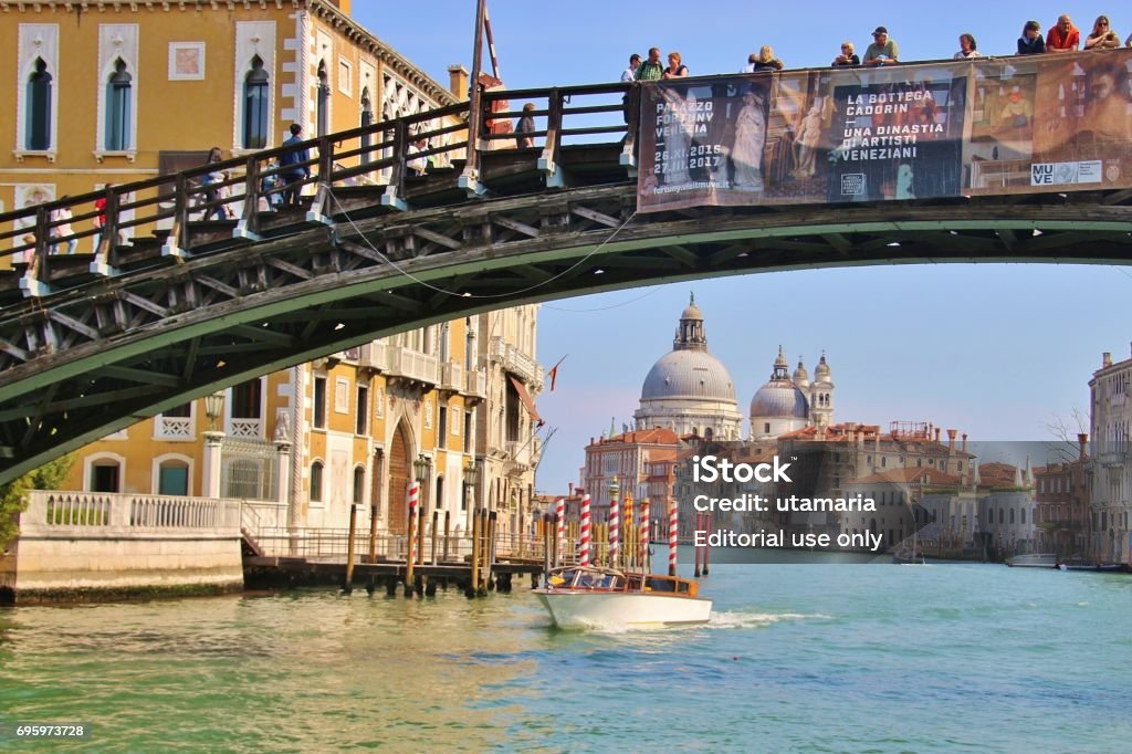 The bridge Ponte dell Accademia, Venice, Italy. Venice, Italy - April 4, 2017: The bridge Ponte dell Accademia with tourists on it, on the Grand Canal in Venice. In the background the baroque church Santa Maria della Salute. Europe. Accademia - Venice Stock Photo