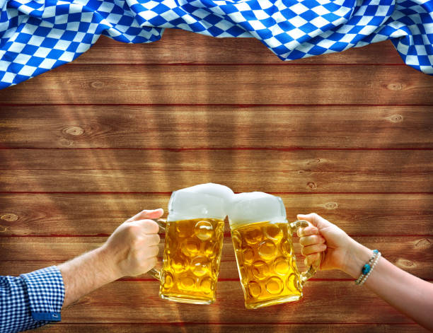 Hands holding up beer mugs under Bavarian flag Cheers! Hands holding up beer mugs under Bavarian flag on wooden background bavarian flag stock pictures, royalty-free photos & images