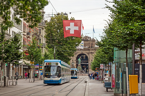 Zurich, Switzerland - June 10, 2017: Shopping promenade called Bahnhofstrasse, inner city of Zurich. Tram / train with swiss flag in front.