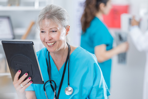 Smiling Caucasian senior doctor uses a digital tablet to video chat with colleague.