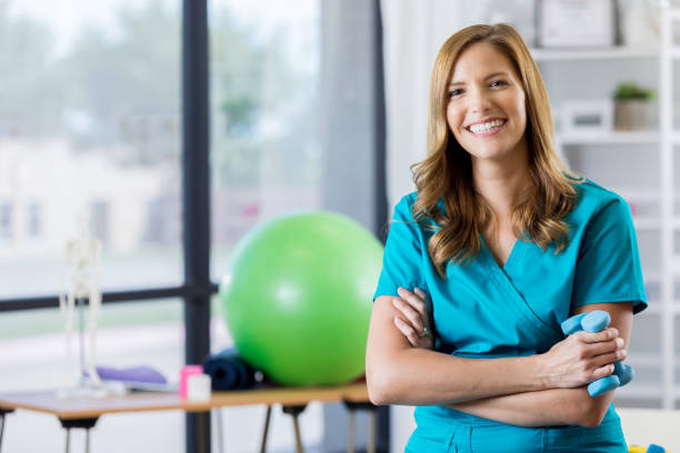 Portrait of beautiful physical therapist Cheerful mid adult physical therapist smiles confidently in a gym. She is holding hand weights. physical therapist stock pictures, royalty-free photos & images