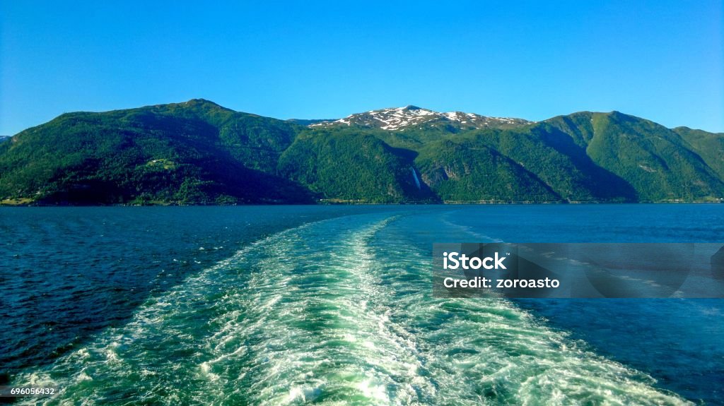Behind a ship in Flam, Norway, Scandinavia, Europe Flam, Norway - June 16, 2014: View from the stern of a cruise ship at sea with the mountains in the background. Cruise Ship Stock Photo