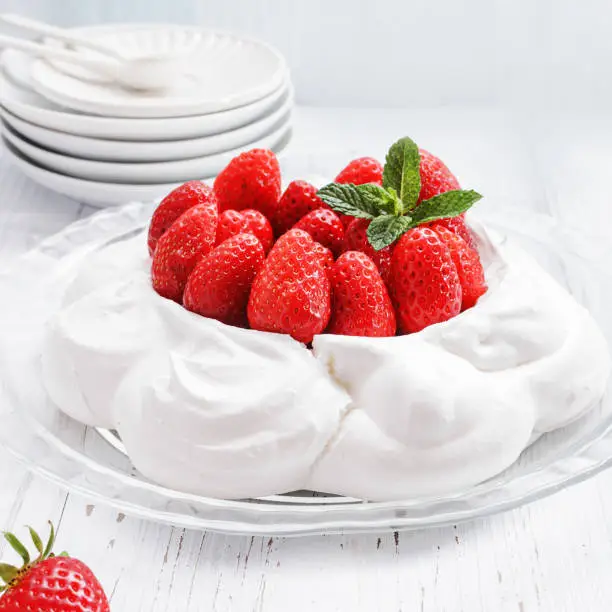 Photo of Pavlova - meringue cake with  fresh strawberries  on  glass plate on old vintage  white wood  background. Top view, copy space, close up, selective focus.