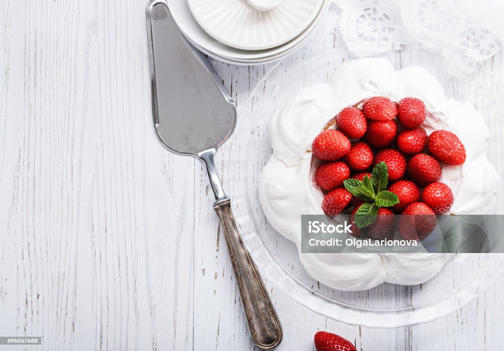 Pavlova - meringue cake with  fresh strawberries on  white wood  background, close up, selective focus. Pavlova - meringue cake with  fresh strawberries  on  glass plate on old vintage  white wood  background. Top view, copy space, close up, selective focus. Australia Stock Photo