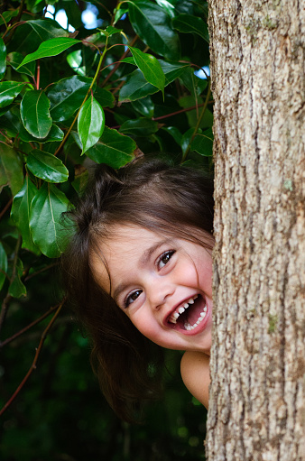Cute little girl is playing hide and seek outdoors.