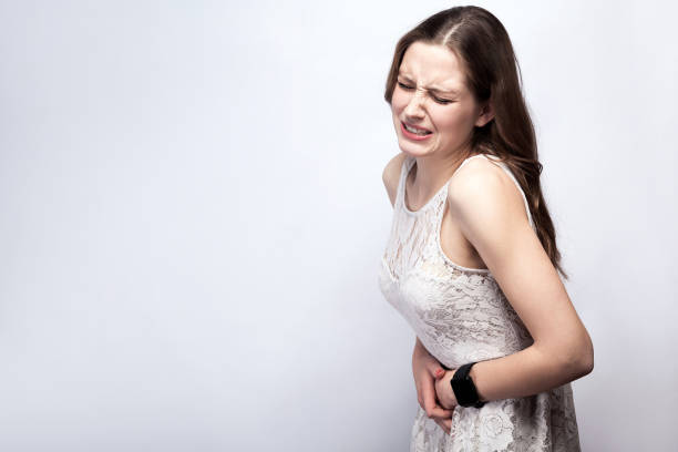 woman with stomach pain Portrait of beautiful woman with freckles and white dress and smart watch with stomach pain on silver gray background. healthcare and medicine concept. tetanospasmin stock pictures, royalty-free photos & images