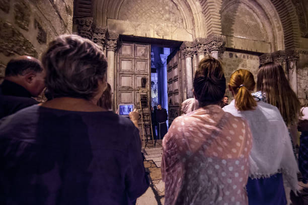 Ritual of closing doors of the Church of Holy Sepulchre Jerusalem, Israel - July 12, 2014: Pilgrims wait for a ritual of closing doors of the Church of Holy Sepulchre. Muslim key holder locks the doors while christian monks wait to be handed a ladder. According to tradition the doors are locked outside every evening with monks and few pilgrims locked inside for the night. Two Muslim families hold the keys to the Church. Jewish security guards are present during the procedure. east jerusalem stock pictures, royalty-free photos & images