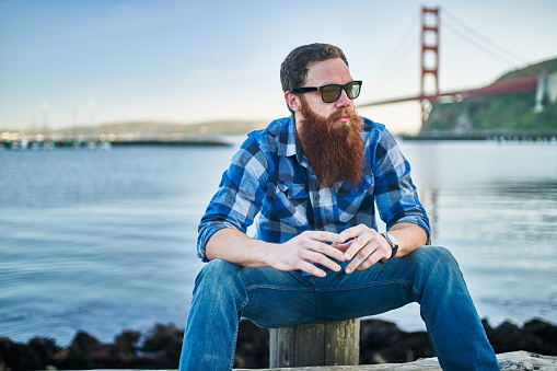 cool bearded hipster chilling out by the bay in front of the golden gate bridge in san francisco