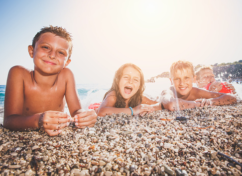 Group of children lying down on sea shore. three boys and a girl, laughing and having fun