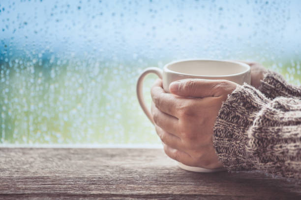 Woman hand holding the cup of coffee or tea on rainy day window background Woman hand holding the cup of coffee or tea on rainy day window background in vintage color tone rainy cafe stock pictures, royalty-free photos & images