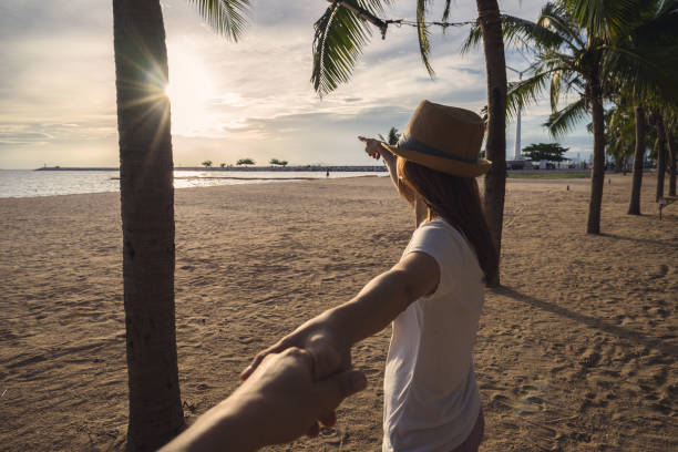 istock young woman holding man's hand on the beach 696124544