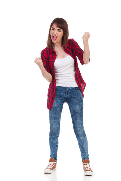 Young Woman Clenches Her Fists And Screams Young woman in unbuttoned red lumberjack shirt and jeans clenches her fists and screams. Full length studio shot isolated on white. legs apart stock pictures, royalty-free photos & images